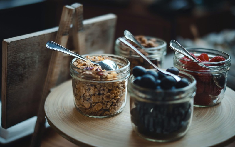 granola and fruit filled jars with spoons on a table