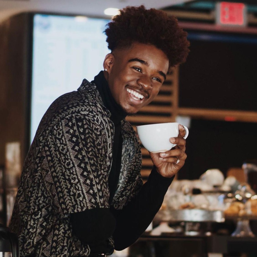 young man smiles while holding a cup of coffee in coffee shop